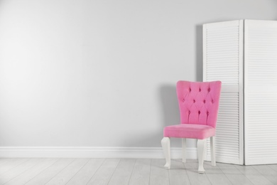 Stylish pink chair and folding screen near white wall. Space for text