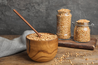 Photo of Uncooked green buckwheat grains in bowl on wooden table