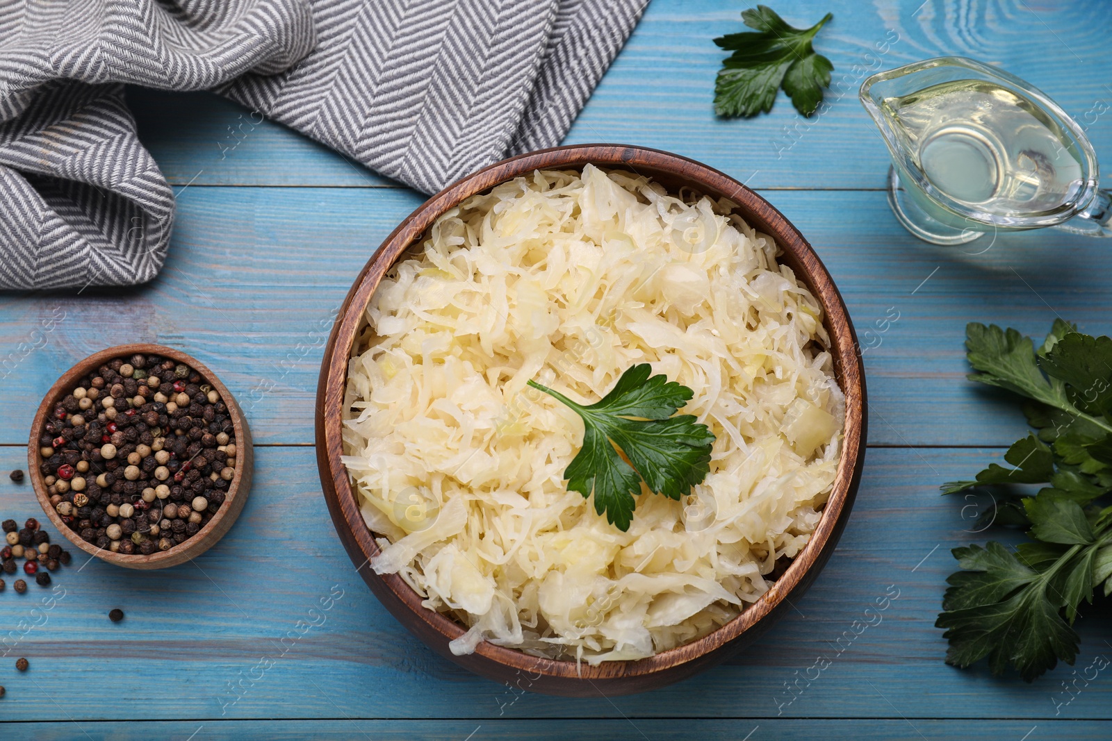 Photo of Bowl of tasty sauerkraut and ingredients on light blue wooden table, flat lay