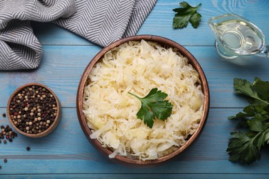 Photo of Bowl of tasty sauerkraut and ingredients on light blue wooden table, flat lay