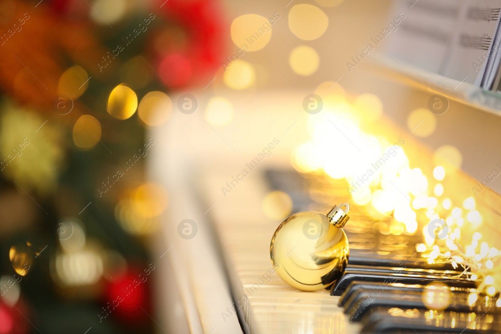 Photo of Beautiful golden bauble and fairy lights on piano keys, space for text. Christmas music