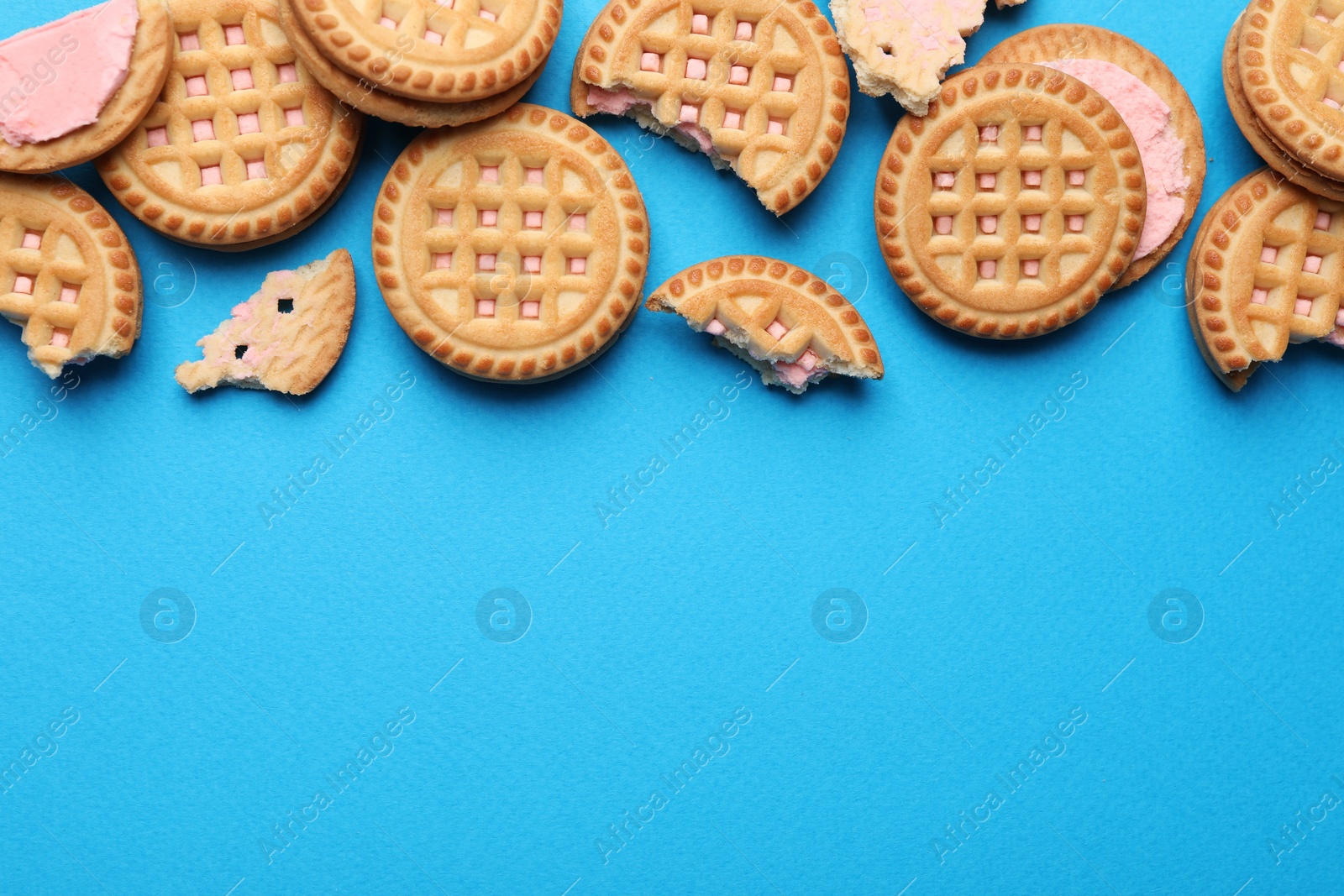 Photo of Tasty sandwich cookies with cream on light blue background, flat lay. Space for text