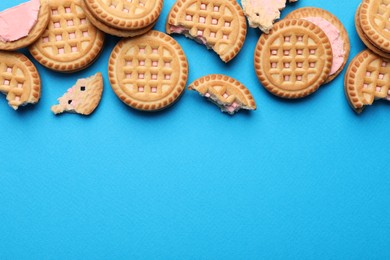 Photo of Tasty sandwich cookies with cream on light blue background, flat lay. Space for text