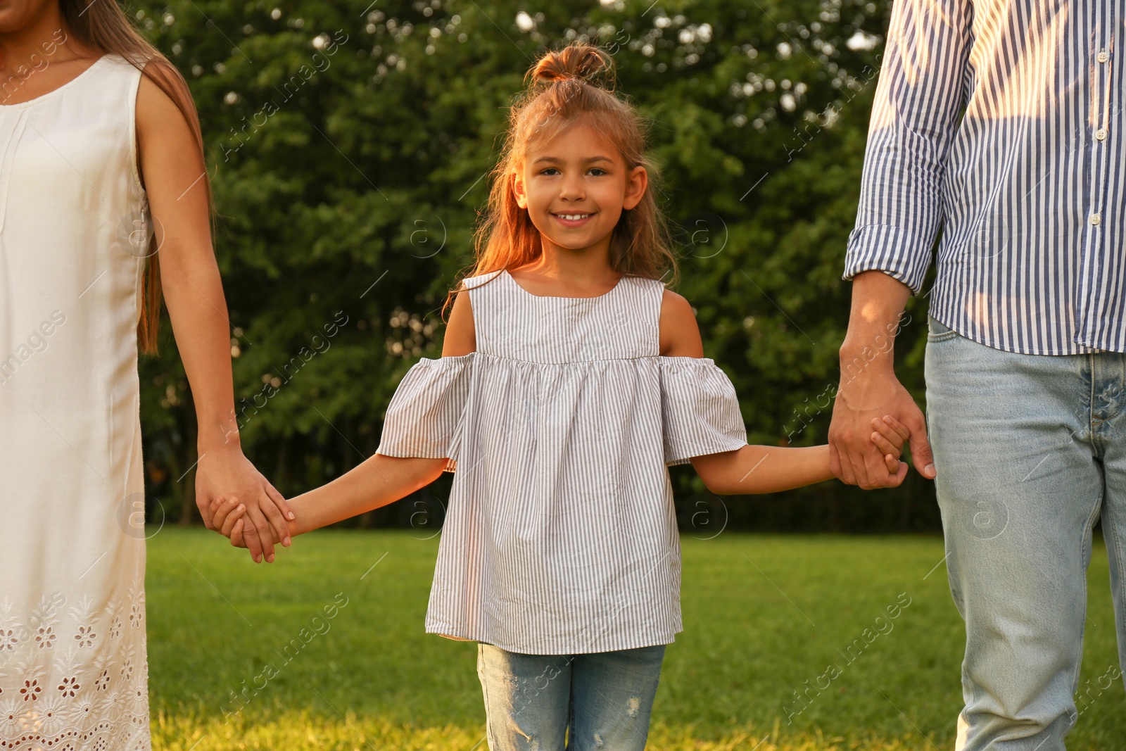 Photo of Little girl and her parents holding hands in park. Happy family