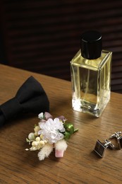 Photo of Wedding stuff. Stylish boutonniere, perfume bottle, bow tie and cufflinks on wooden table, closeup