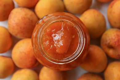 Jar of delicious jam and fresh ripe apricots on white background, flat lay. Fruit preserve