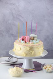 Photo of Delicious cake decorated with macarons, marshmallows and candles served on white table against grey background