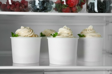 Cups with tasty frozen yogurt on fridge shelf