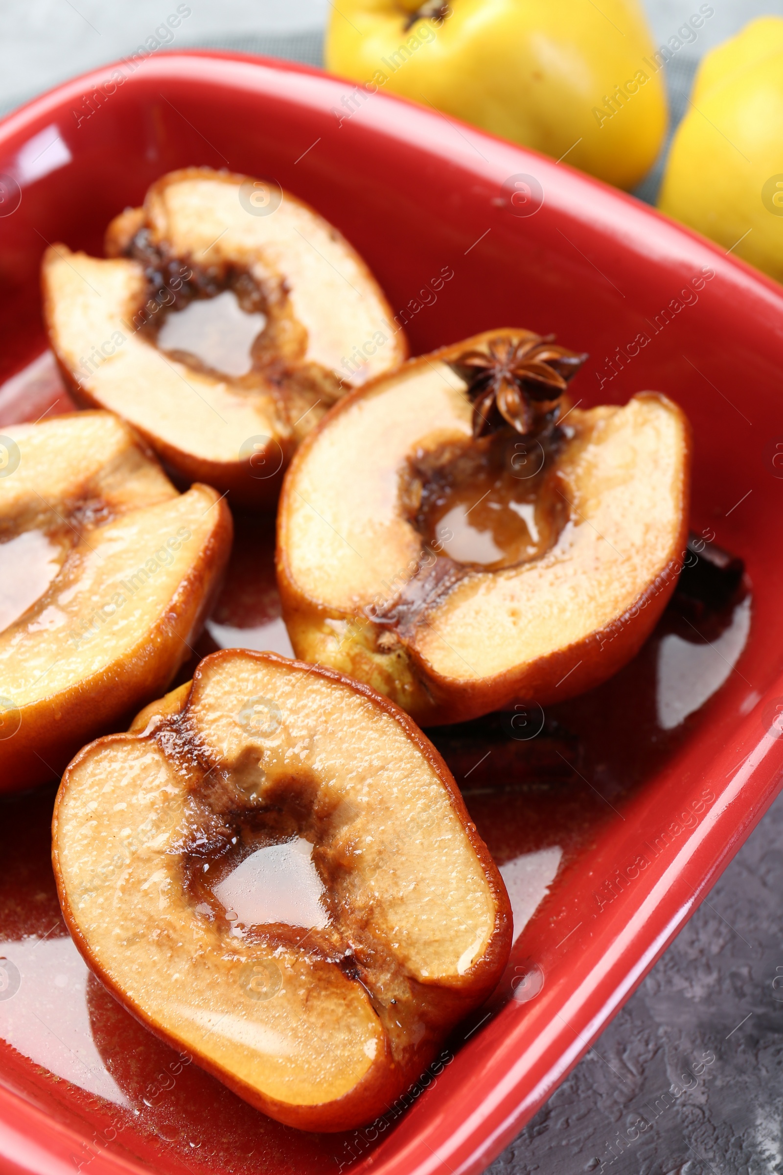 Photo of Tasty baked quinces with honey in dish on grey textured table, closeup