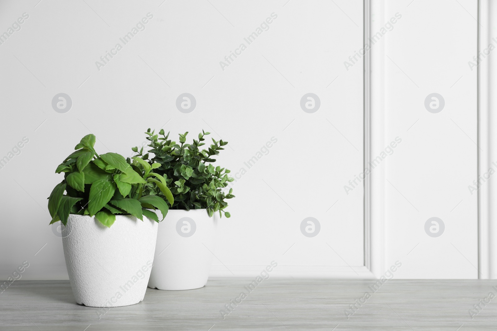 Photo of Different artificial potted herbs on white wooden table near wall, space for text