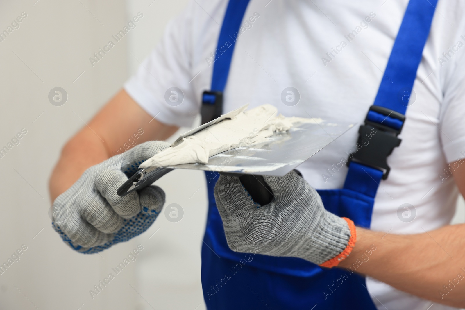 Photo of Worker with putty knives and plaster near wall, closeup