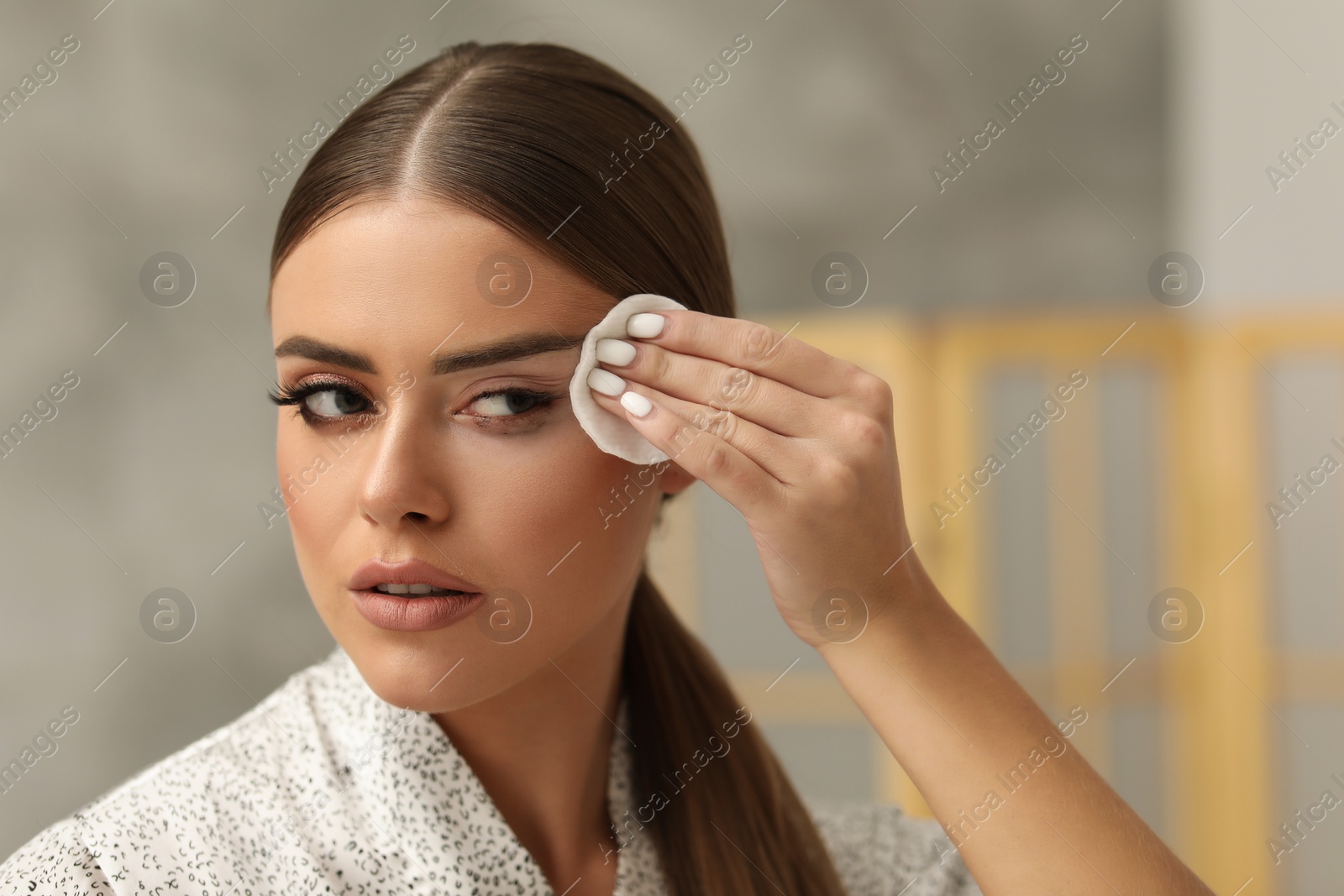 Photo of Beautiful woman removing makeup with cotton pad indoors