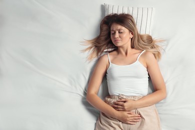 Photo of Young woman suffering from menstrual pain in bed, top view. Space for text