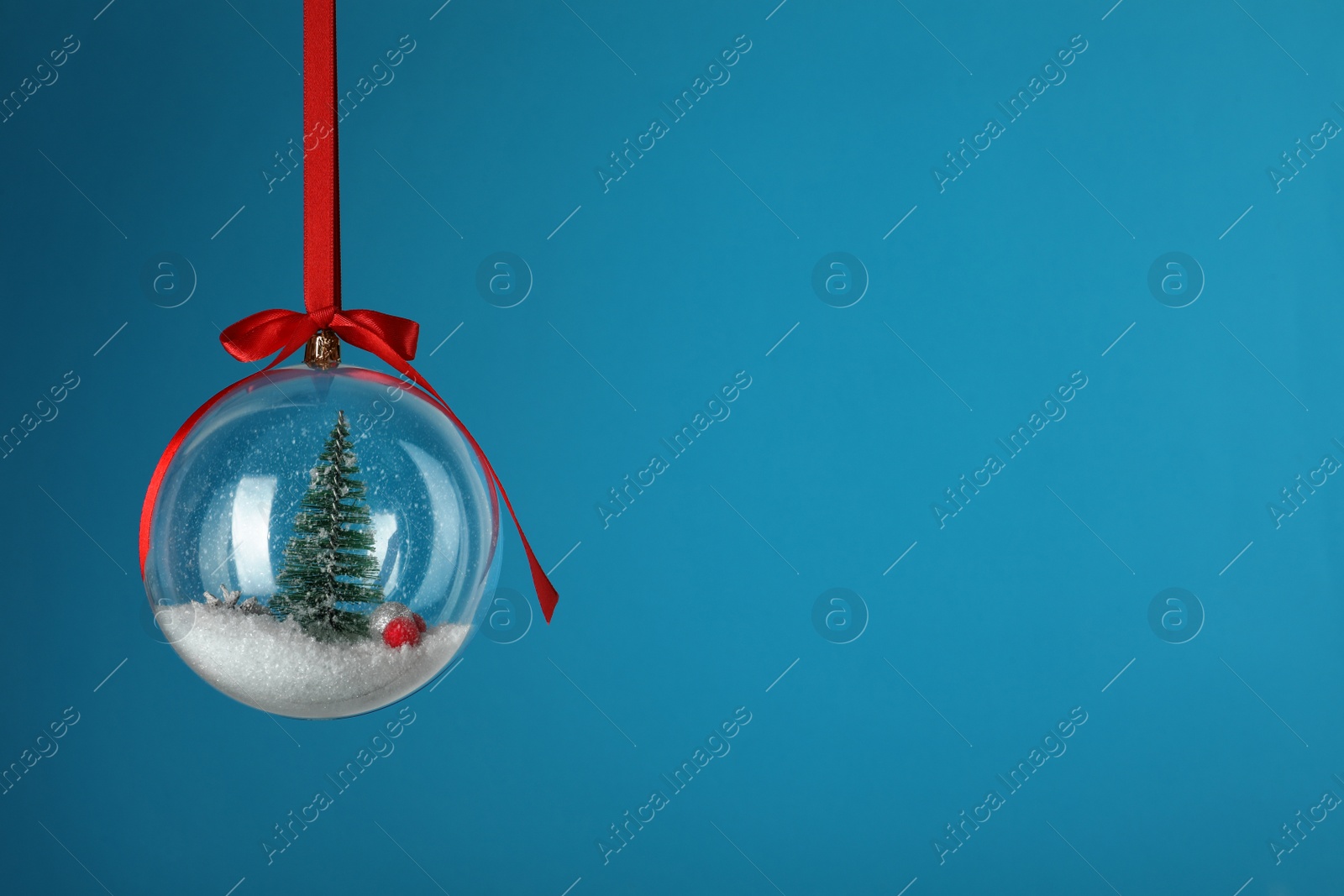 Photo of Beautiful Christmas snow globe hanging on blue background, space for text
