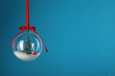 Photo of Beautiful Christmas snow globe hanging on blue background, space for text