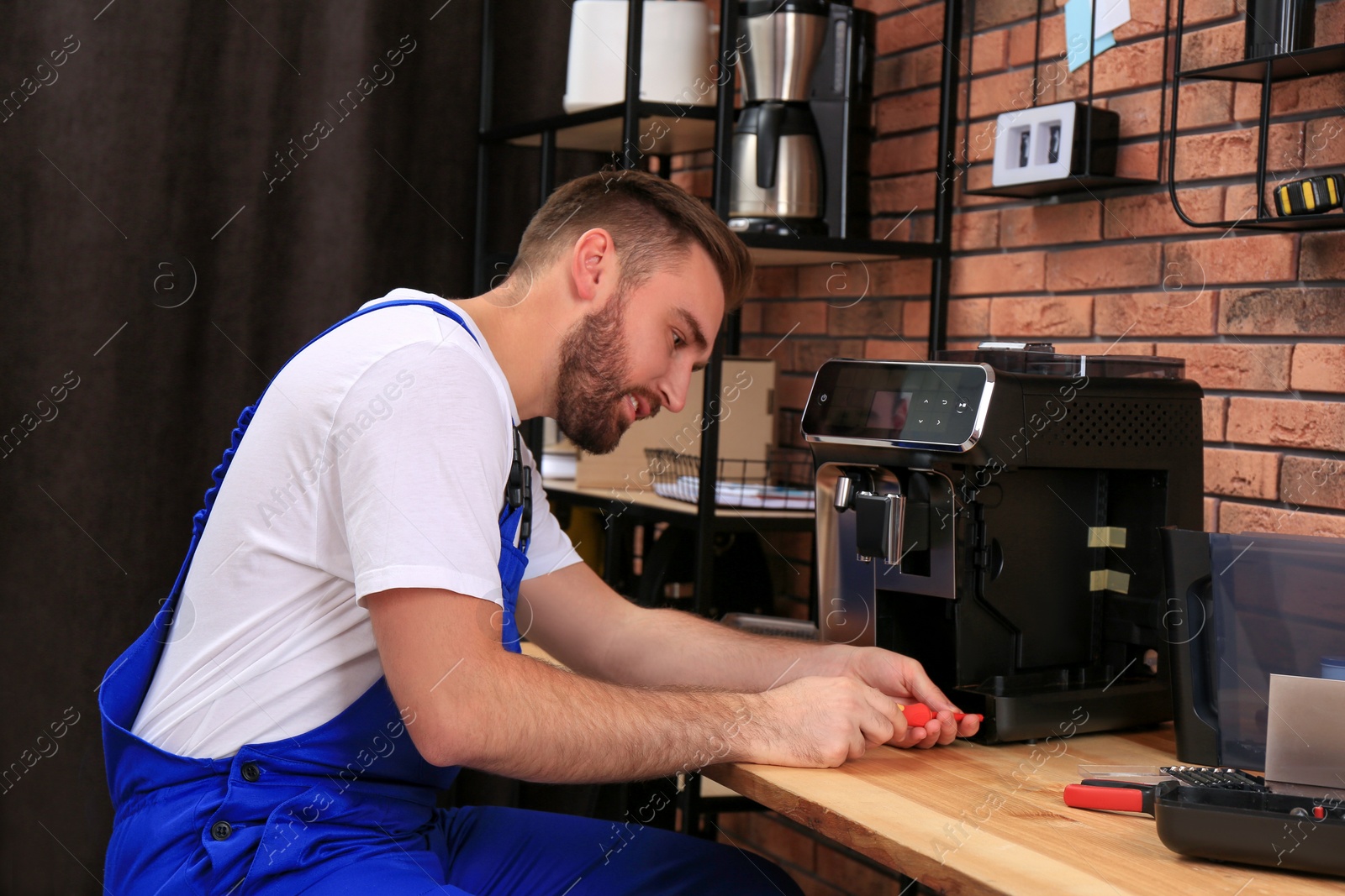 Photo of Repairman with screwdriver fixing coffee machine at table indoors