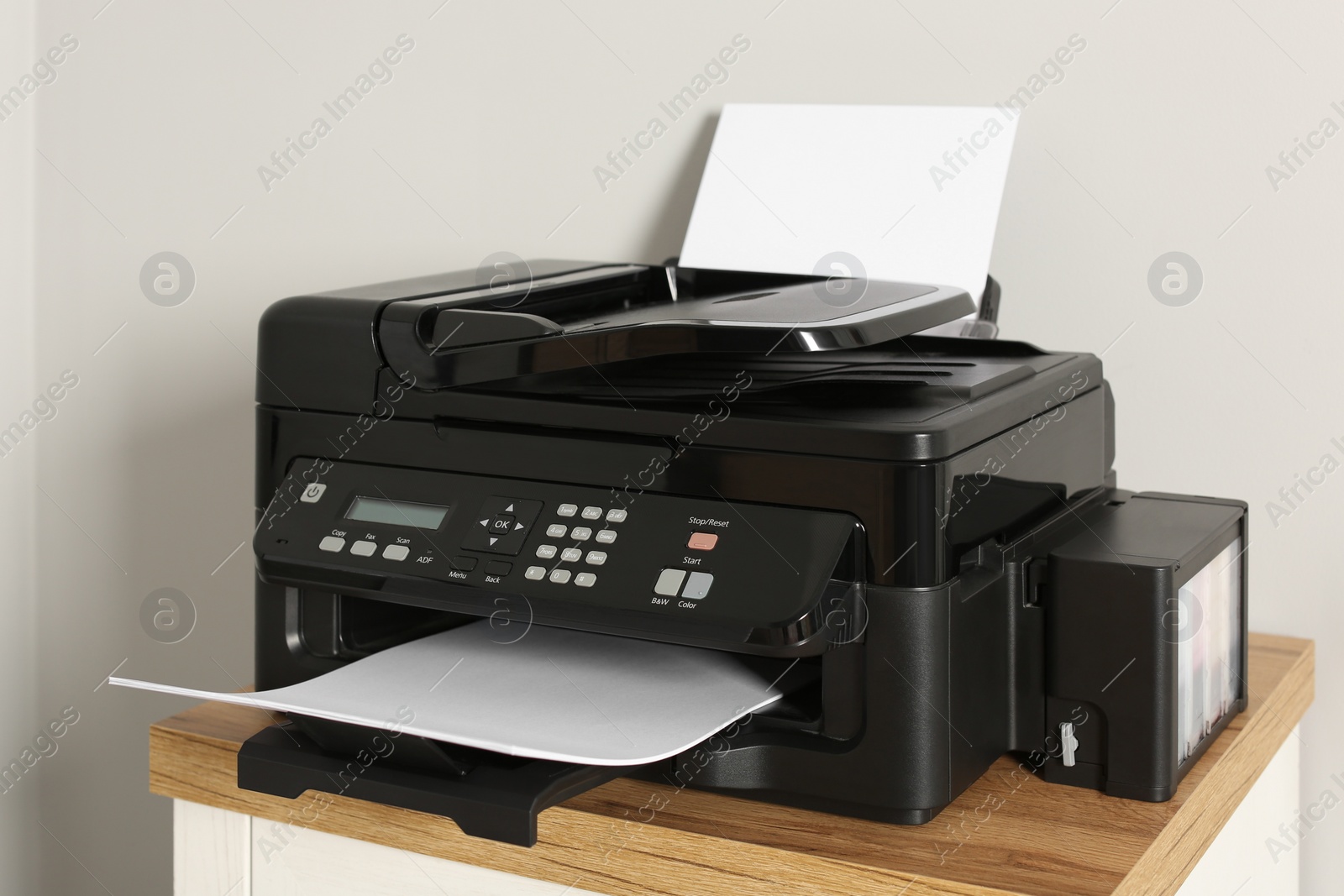 Photo of Modern printer with paper on chest of drawers indoors