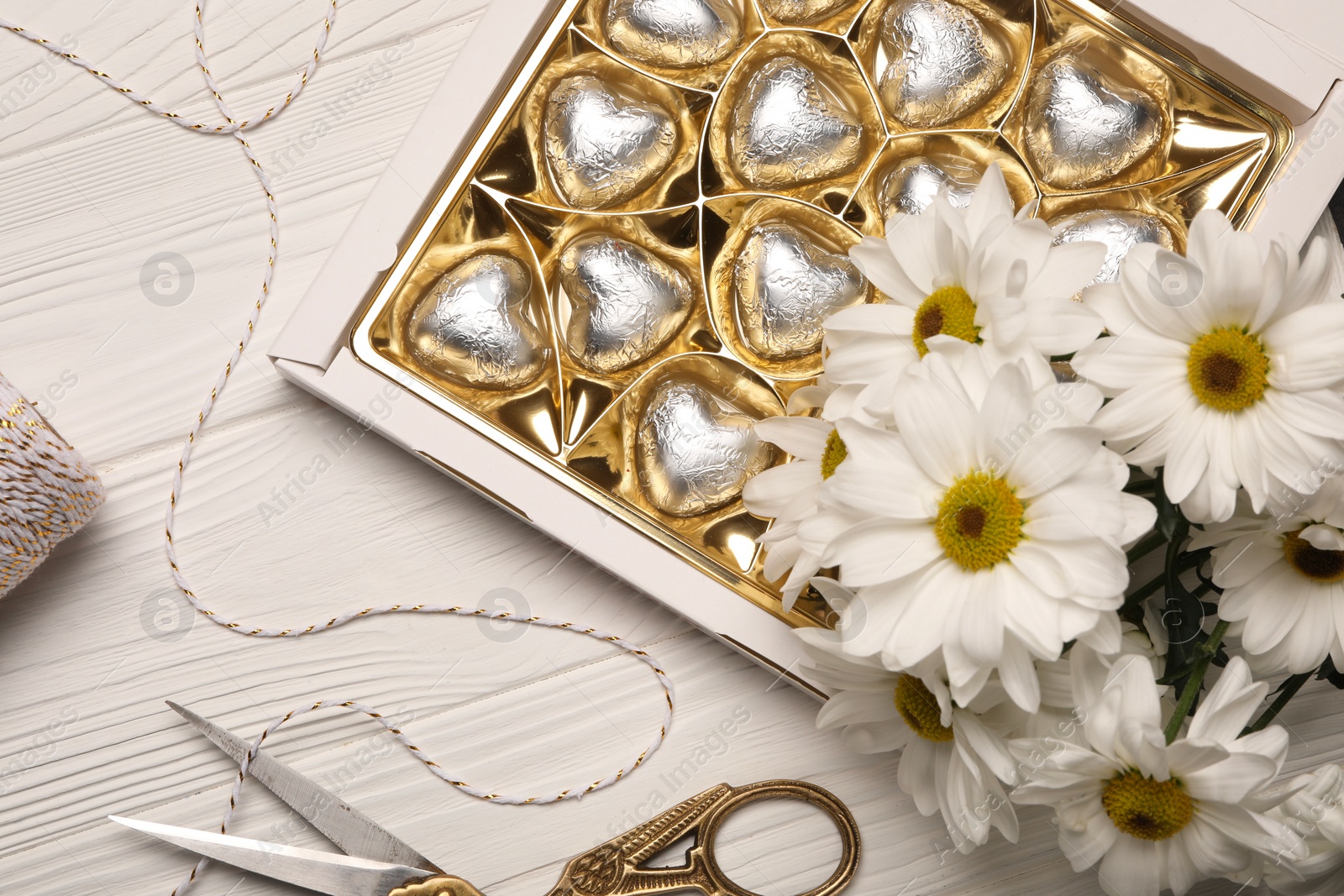 Photo of Delicious heart shaped chocolate candies, scissors and twine on white wooden table, flat lay