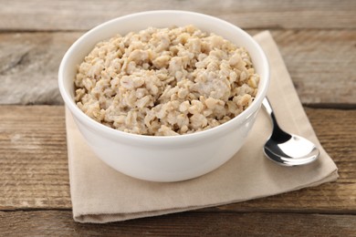 Photo of Tasty boiled oatmeal in bowl and spoon on wooden table, closeup