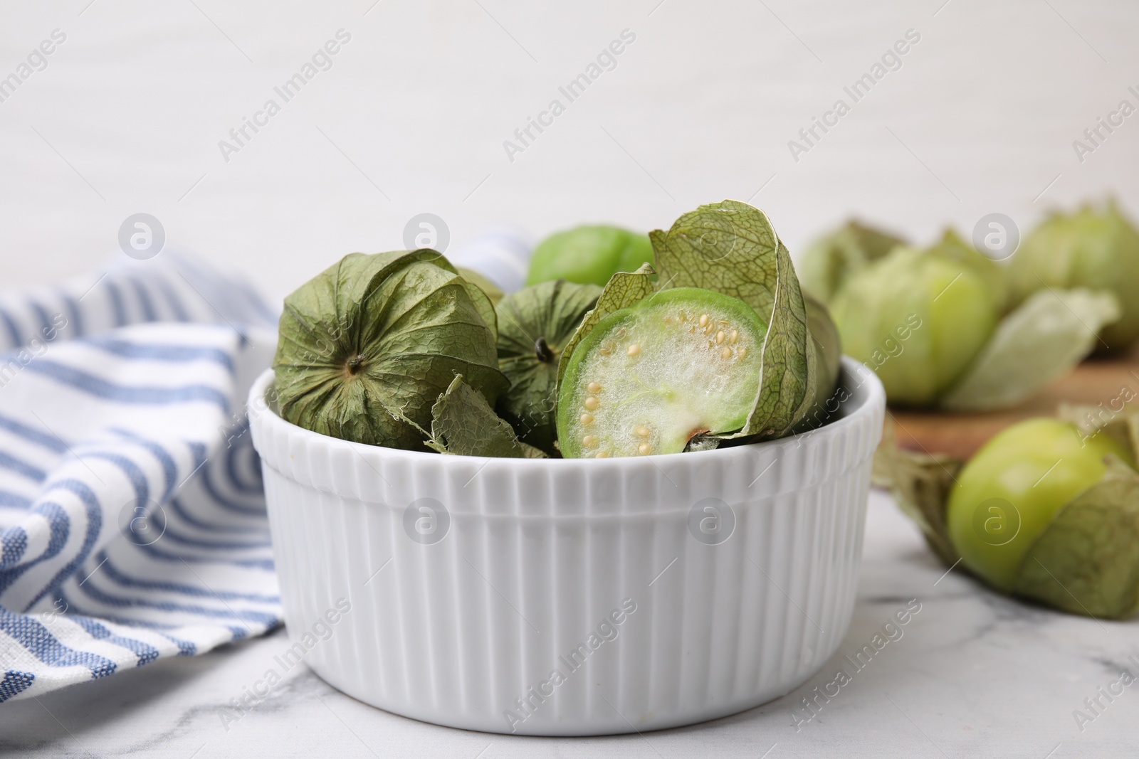 Photo of Fresh green tomatillos with husk in bowl on light marble table, closeup