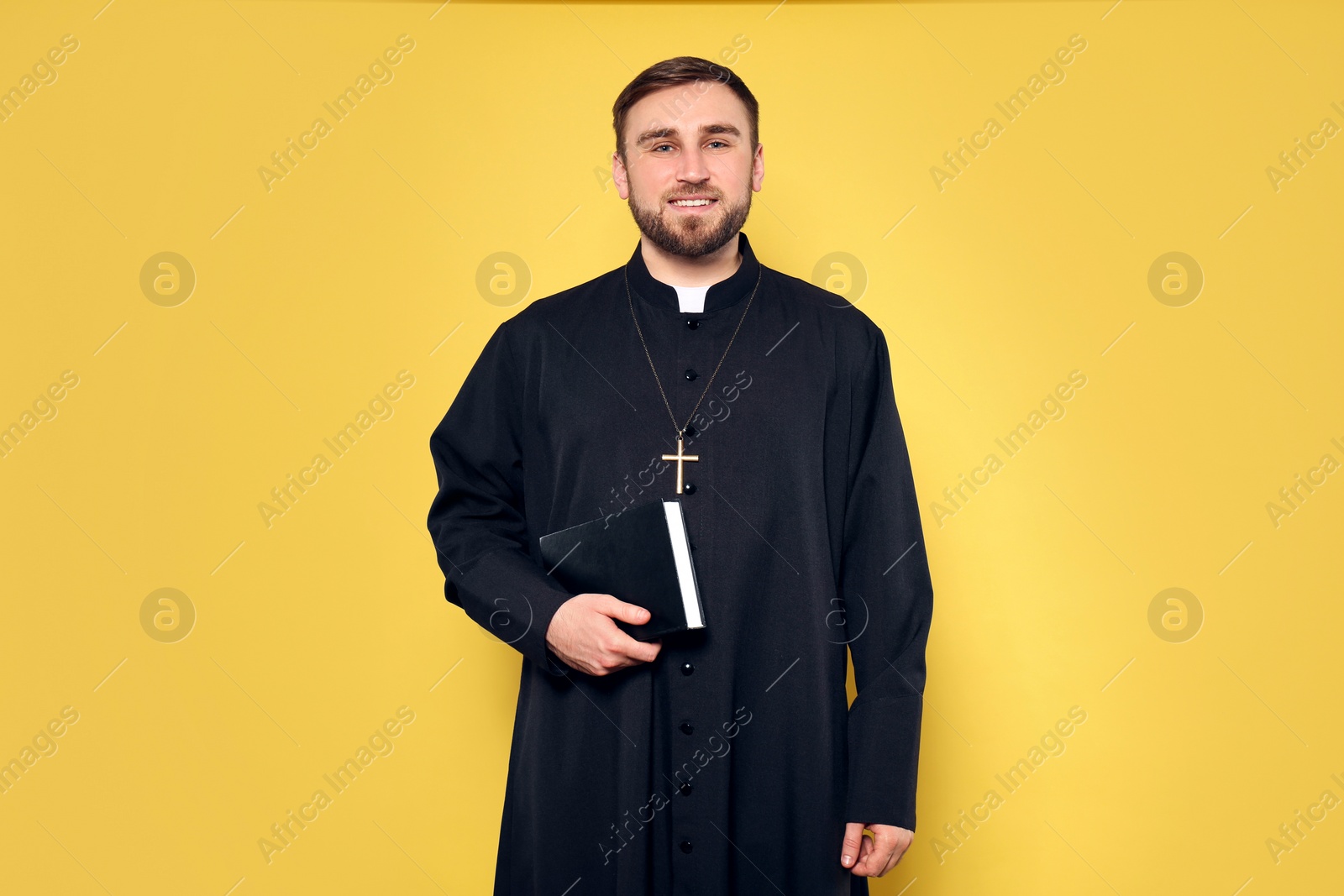 Photo of Priest in cassock with Bible on yellow background