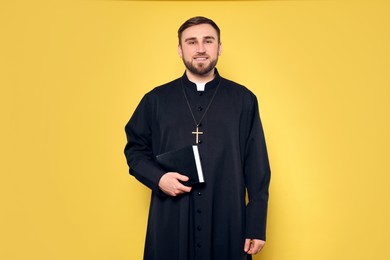 Priest in cassock with Bible on yellow background