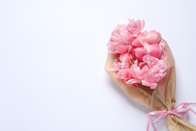 Beautiful bouquet of pink peonies wrapped in paper on white background, top view