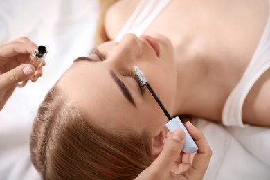 Beautician applying oil onto woman's eyelashes in salon