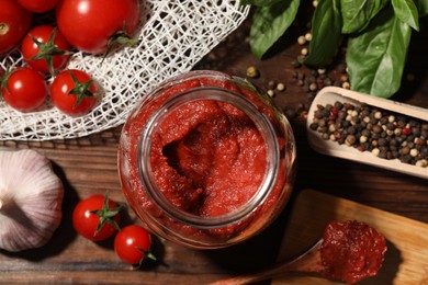 Jar of tasty tomato paste and ingredients on wooden table, flat lay