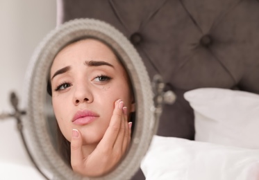 Young woman with eyelash loss problem looking in mirror indoors