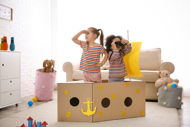 Photo of Cute little children playing with cardboard ship and binoculars at home