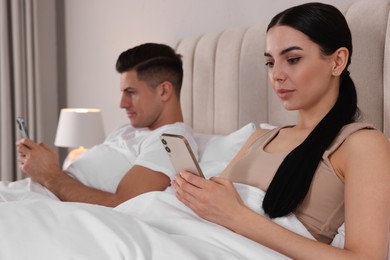 Photo of Internet addiction. Couple with smartphones in bed indoors