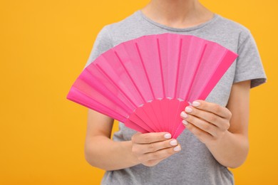 Woman holding hand fan on orange background, closeup
