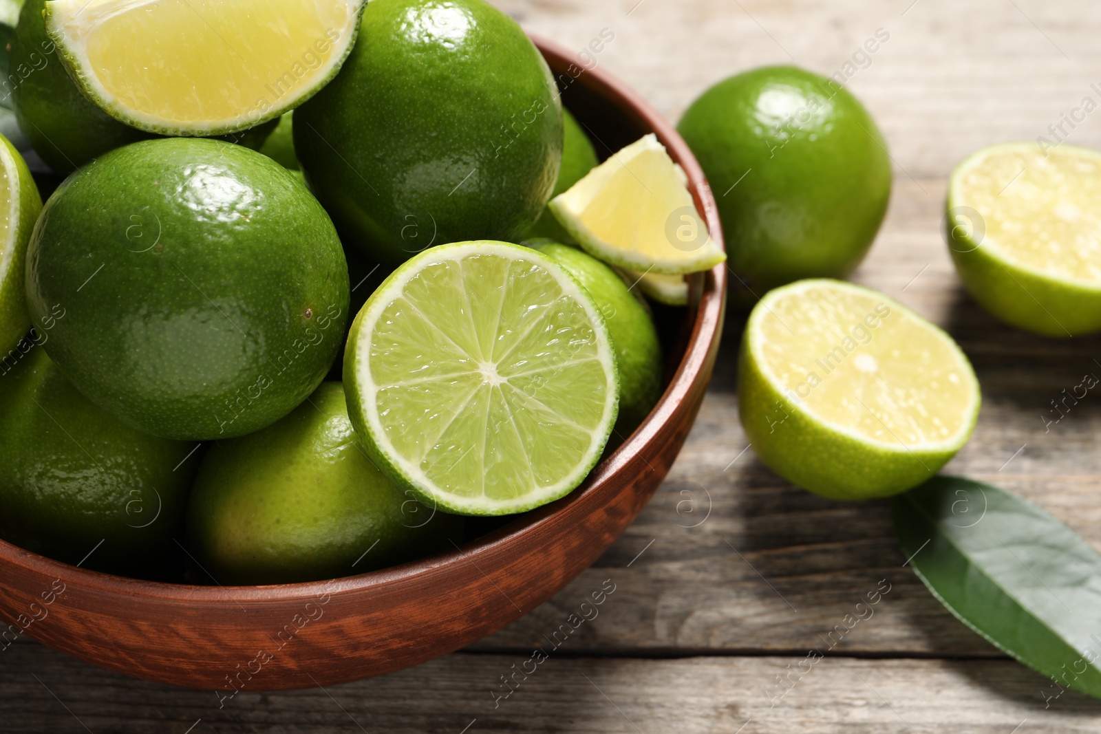 Photo of Tasty ripe limes in bowl on wooden table, closeup