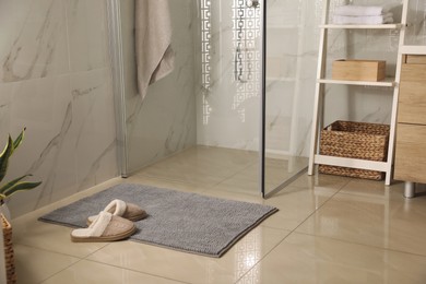 Photo of Soft grey bath mat and slippers on floor in bathroom