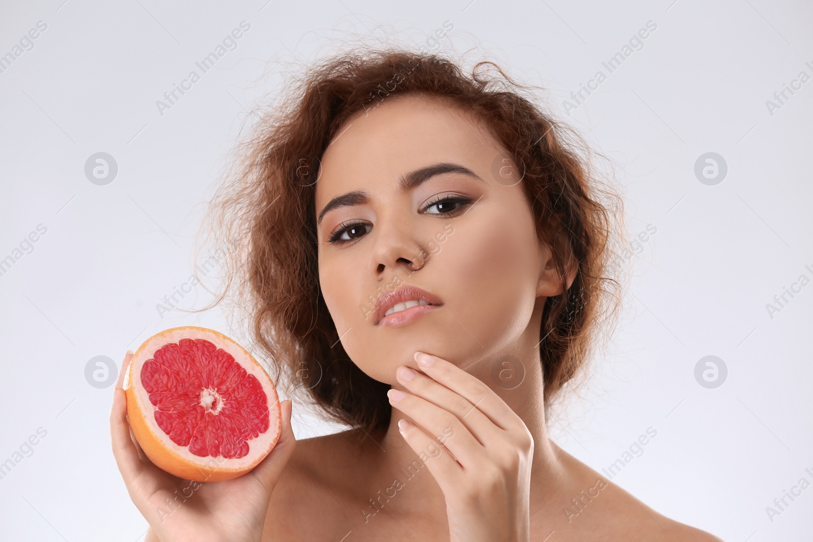 Photo of Beautiful young woman with acne problem holding grapefruit on light background. Skin allergy