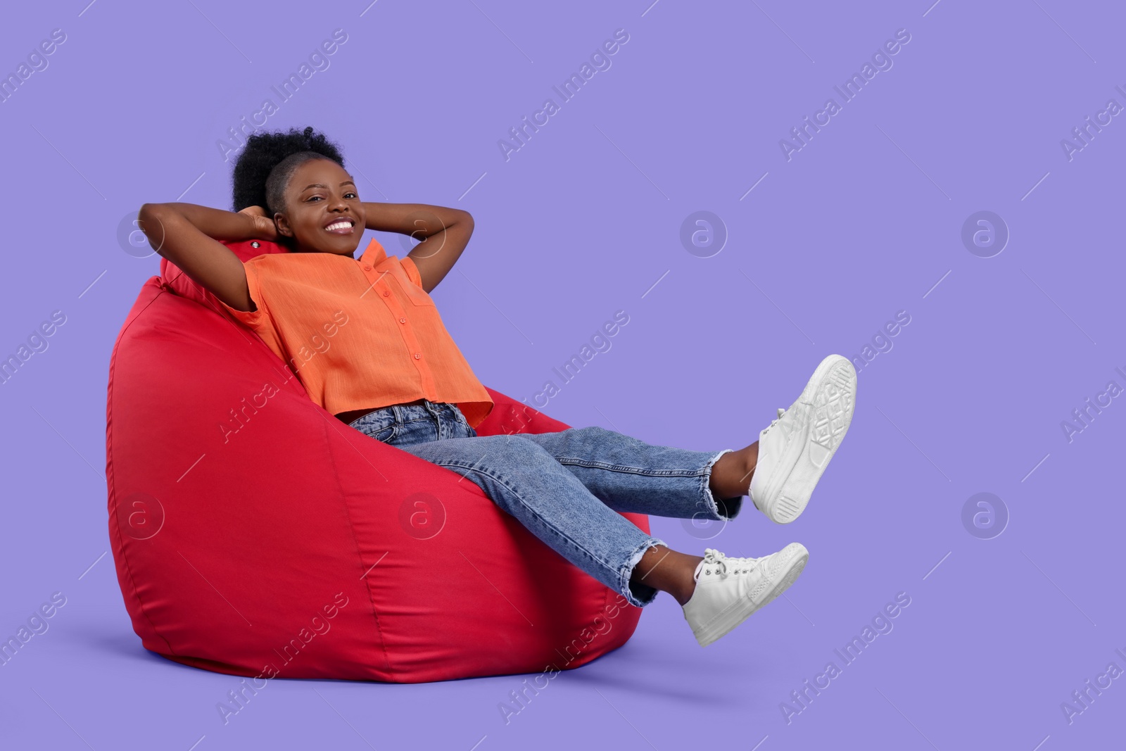 Photo of Beautiful young woman sitting on beanbag chair against purple background. Space for text