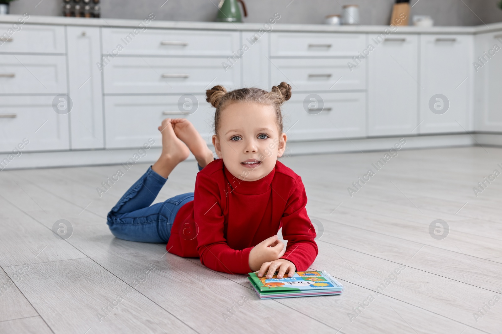 Photo of Cute little girl with book on warm floor in kitchen. Heating system