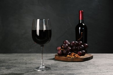 Glass of red wine, bottle, nuts and grapes on grey table