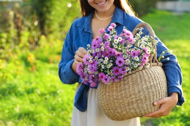 Photo of Woman holding wicker basket with beautiful wild flowers outdoors, closeup