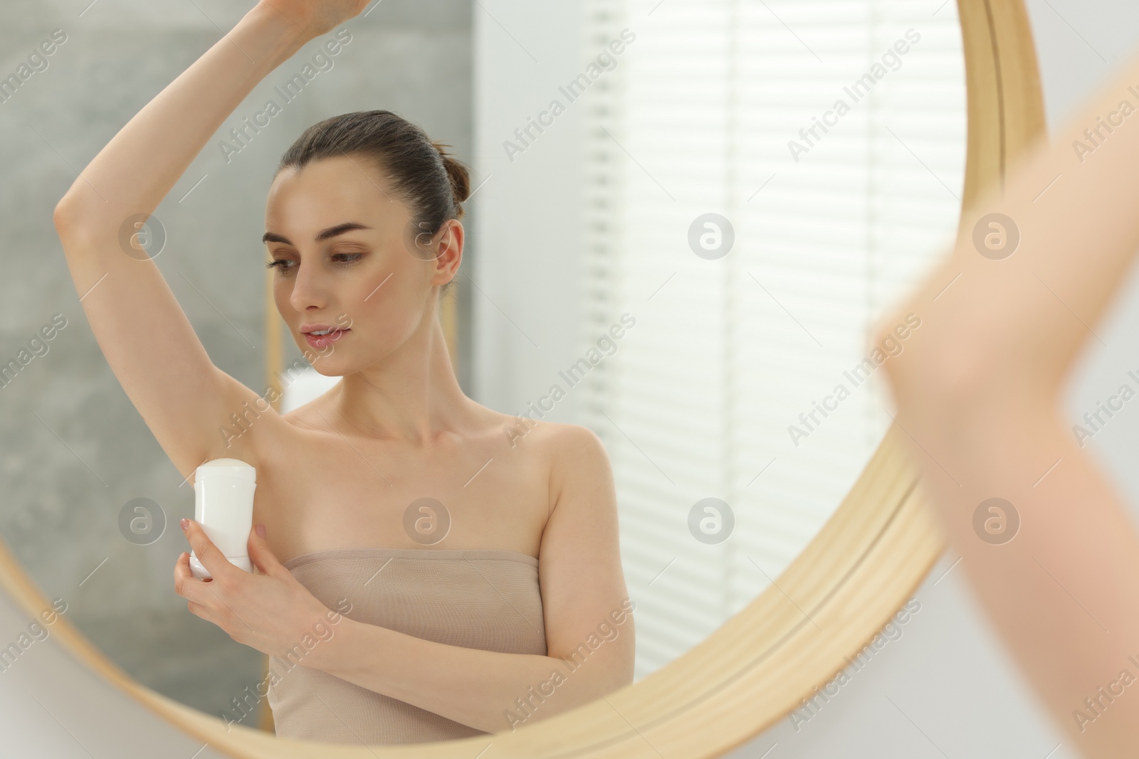 Photo of Beautiful woman applying deodorant near mirror in bathroom