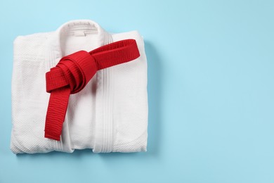 Photo of Red karate belt and white kimono on light blue background, top view. Space for text