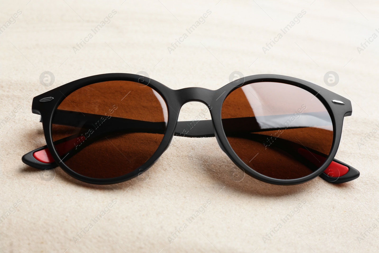 Photo of Stylish sunglasses on white sand. Summer time