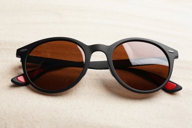 Stylish sunglasses on white sand. Summer time