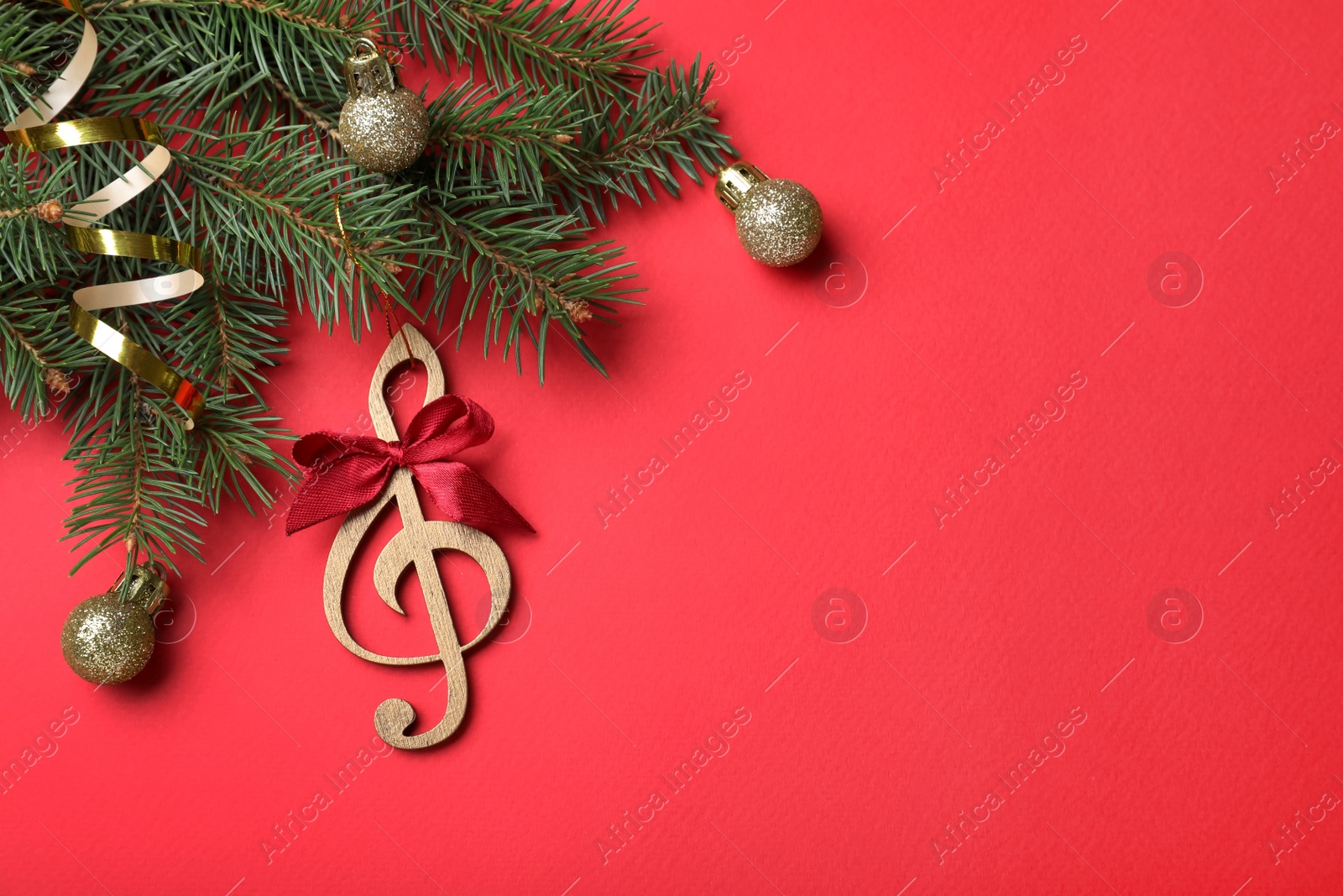 Photo of Top view of fir tree branches with Christmas decor and wooden music note on red background, space for text
