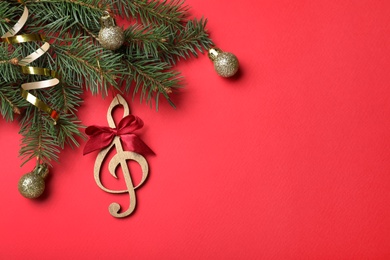 Top view of fir tree branches with Christmas decor and wooden music note on red background, space for text