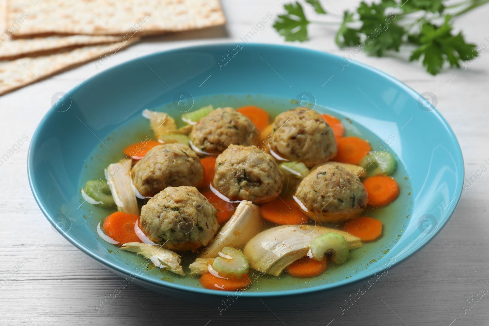 Photo of Bowl of Jewish matzoh balls soup on white wooden table