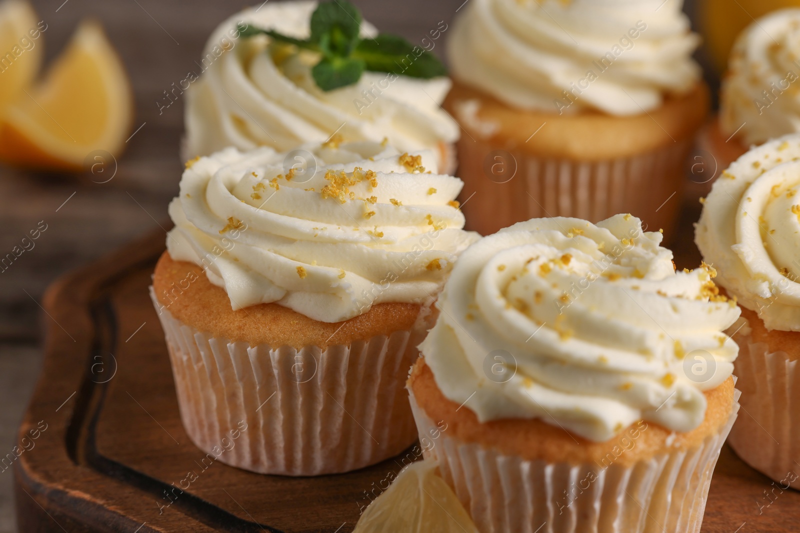 Photo of Delicious cupcakes with white cream and lemon zest on wooden board, closeup
