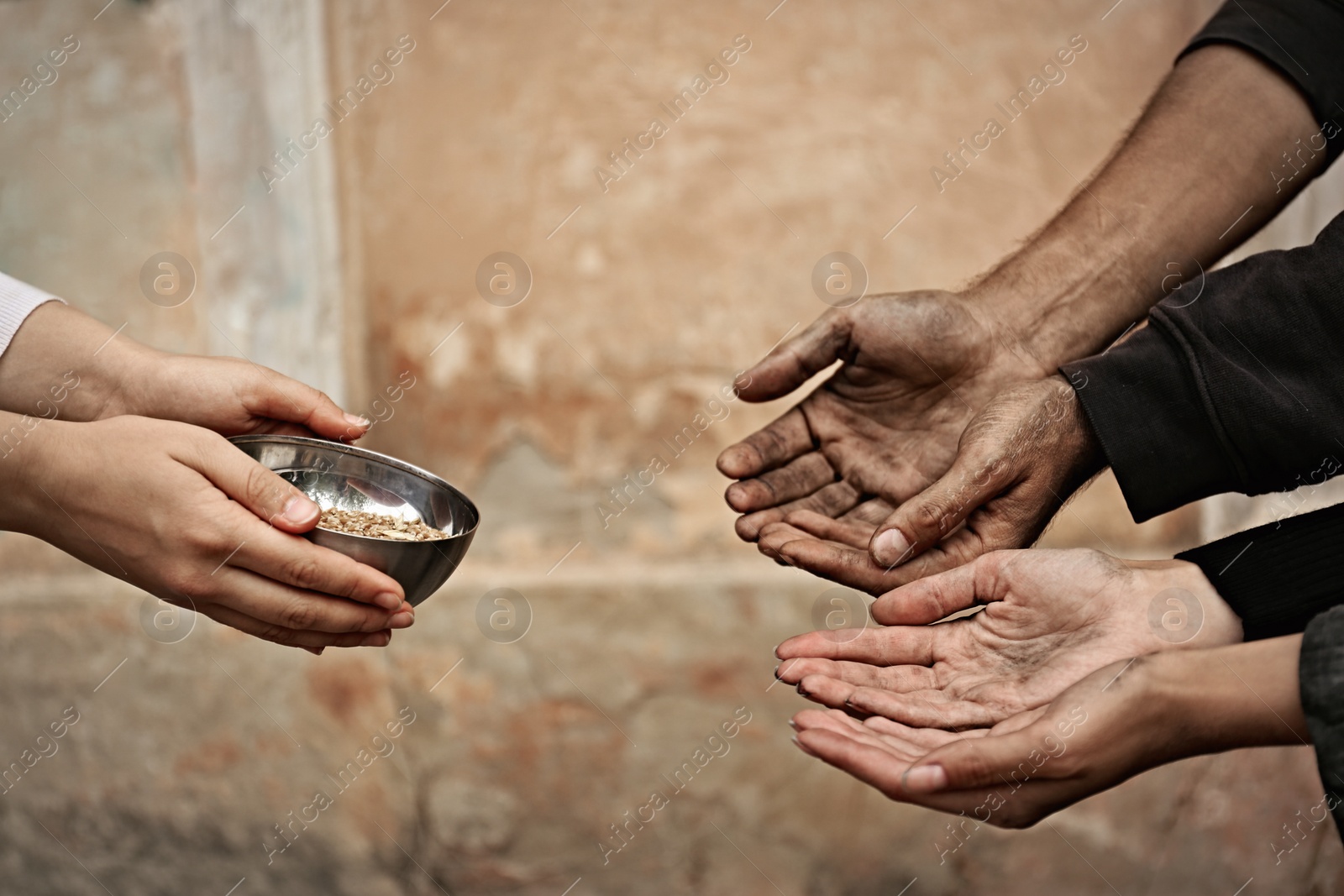 Photo of Woman giving poor homeless people bowl of wheat outdoors, closeup