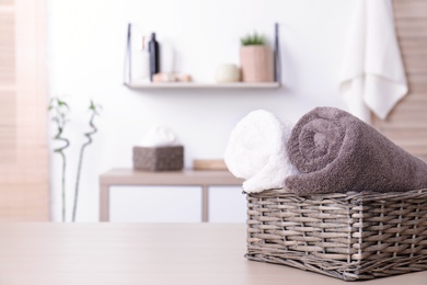 Photo of Basket with rolled fresh towels on table in bathroom. Space for text